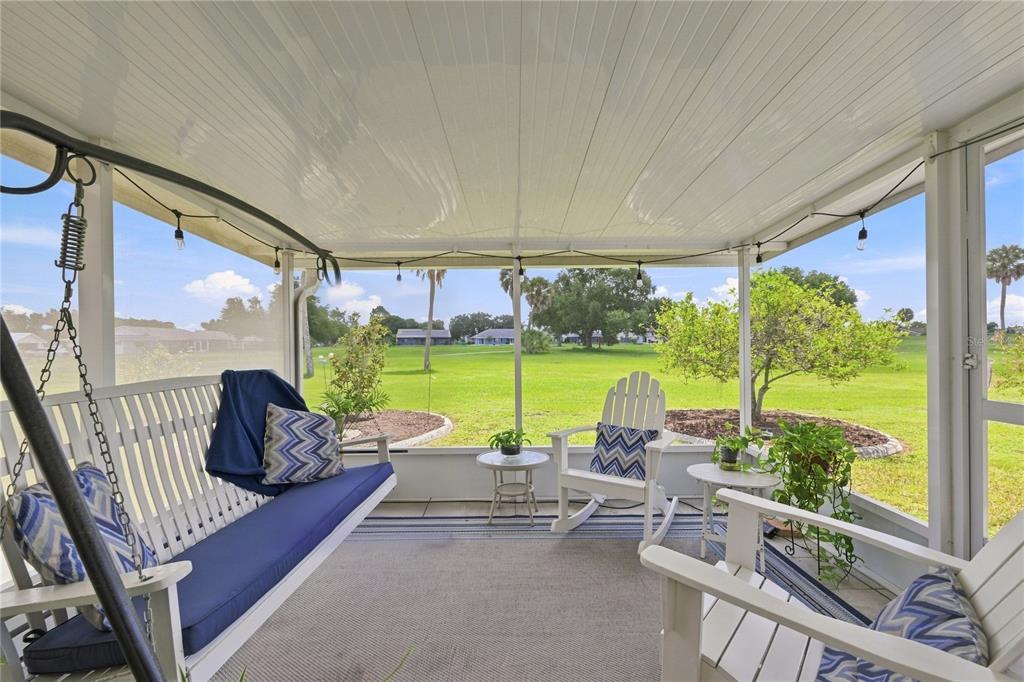 A screened-in porch features a hanging swing, white rocking chairs, and views of a grassy lawn — 1405 HACIENDA DRIVE, SUN CITY CENTER, FL