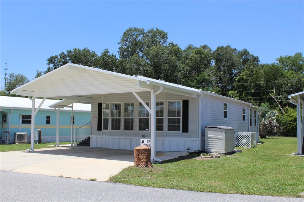 A light gray manufactured home features a large attached carport and a concrete driveway — 12 SADDLEBAG TRAIL, LAKE WALES, FL