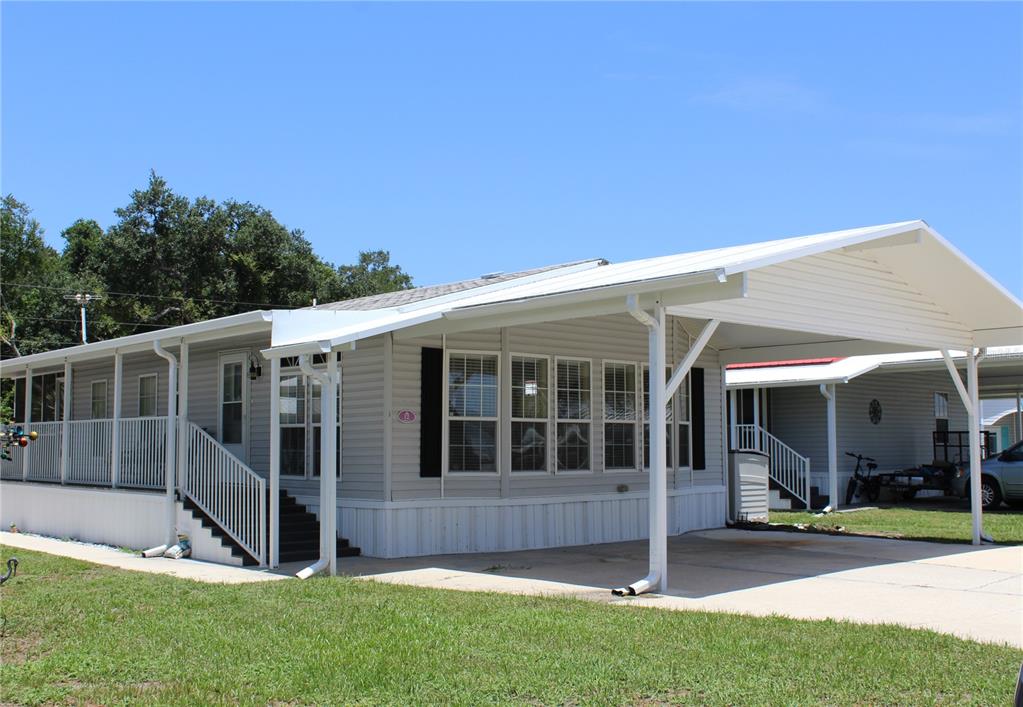 A light-colored manufactured home features a large attached carport and a side deck with railings — 12 SADDLEBAG TRAIL, LAKE WALES, FL