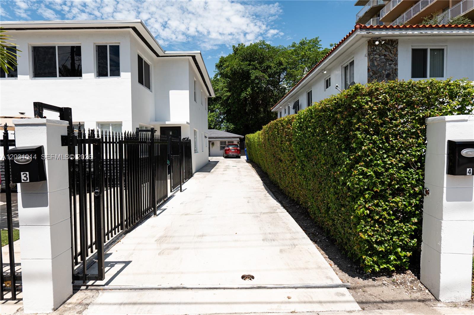 A concrete driveway leads between two white buildings, separated by a black metal fence and hedge — 2240 SW 16th Ct # U, Miami FL 33145, MIAMI, FL