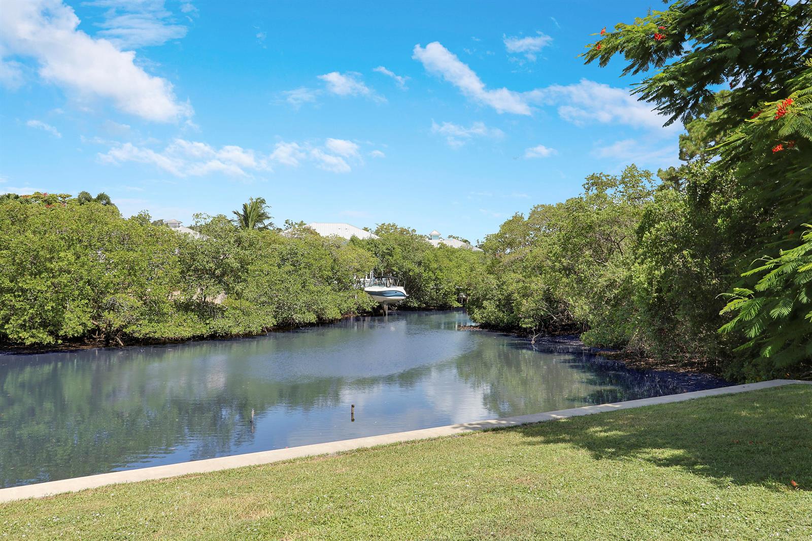 A boat sits in a narrow canal surrounded by lush green trees under a blue sky — 1329 Chippewa Street, Jupiter FL 33458, JUPITER, FL