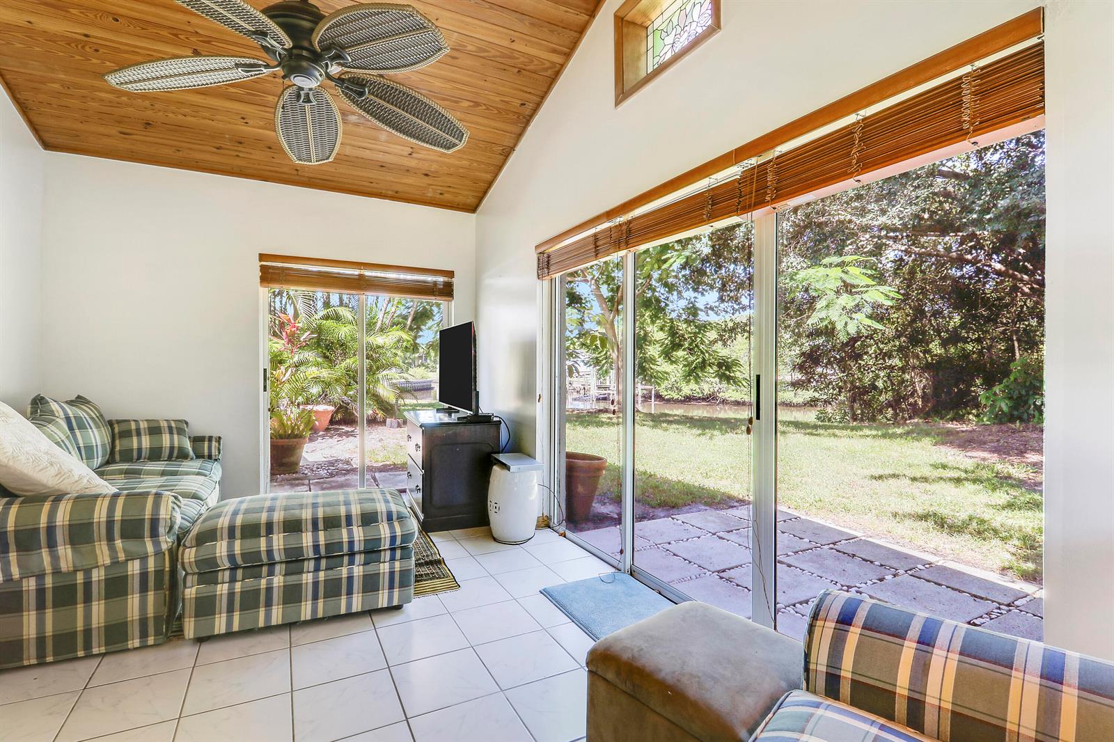 A sunroom with a wood-paneled ceiling, plaid furniture, and sliding glass doors overlooking a yard — 1329 Chippewa Street, Jupiter FL 33458, JUPITER, FL