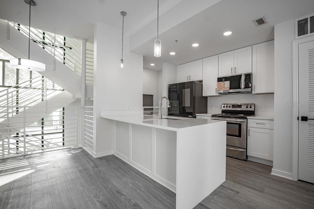 A modern kitchen features white cabinets, stainless steel appliances, a quartz island, and a staircase — 460 E JACKSON STREET UNIT 2, ORLANDO, FL