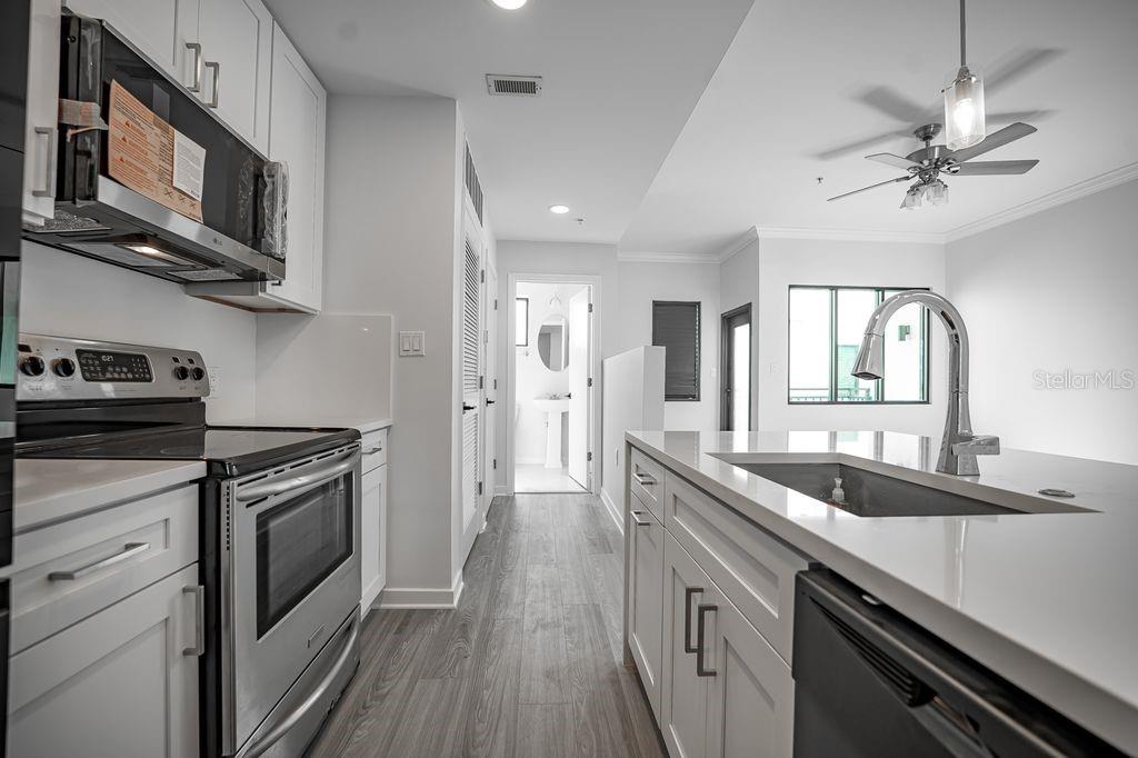 A modern kitchen features white cabinetry, stainless steel appliances, and a central island with sink — 460 E JACKSON STREET UNIT 2, ORLANDO, FL