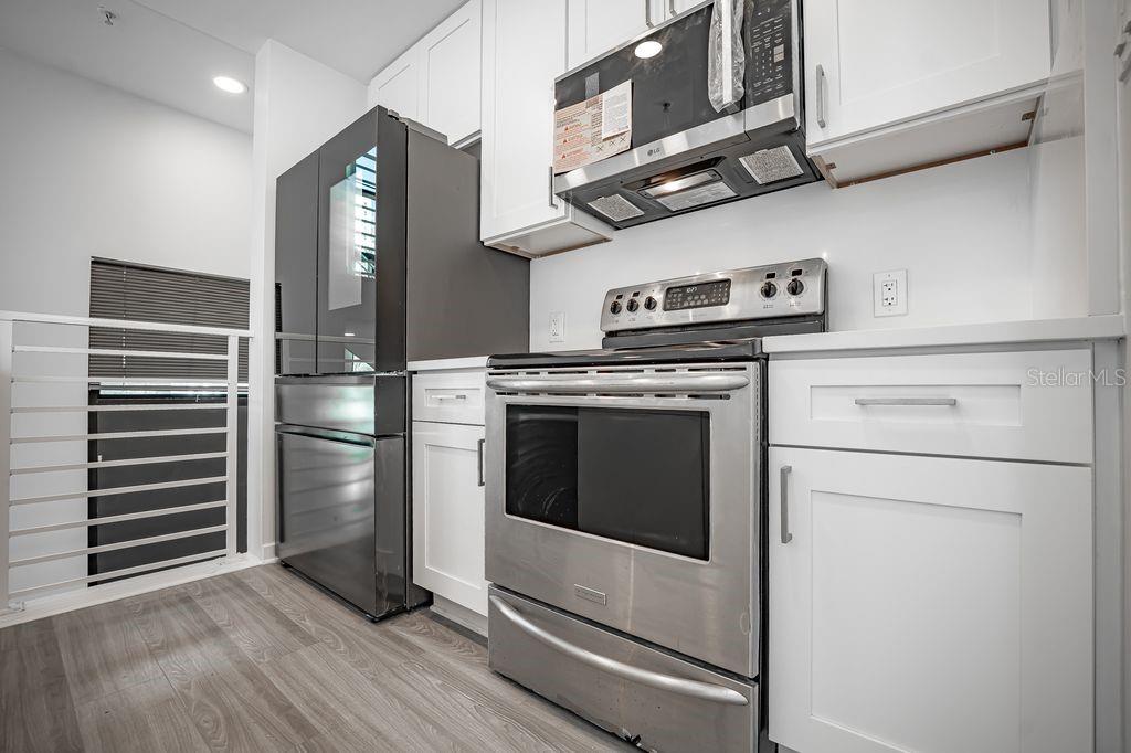 A kitchen features white cabinets, stainless steel appliances, and wood-look flooring — 460 E JACKSON STREET UNIT 2, ORLANDO, FL