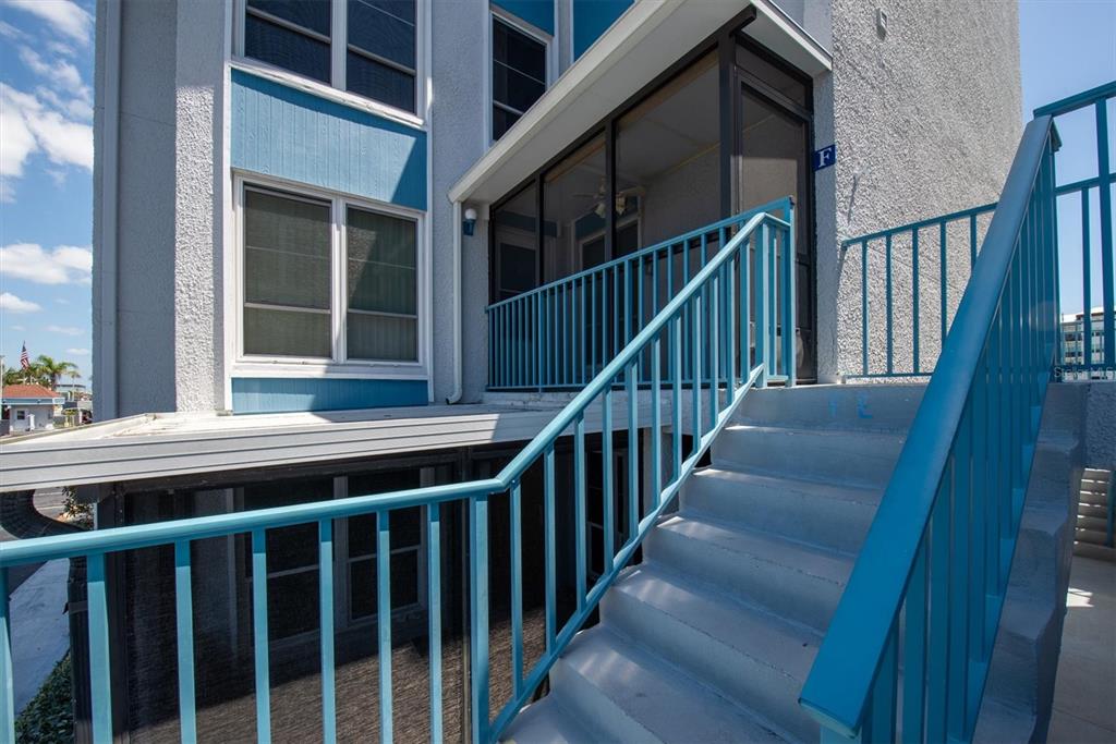 Exterior view of a building with blue railings, a screened-in porch, and concrete stairs — 171 MEDALLION BOULEVARD UNIT F, MADEIRA BEACH, FL