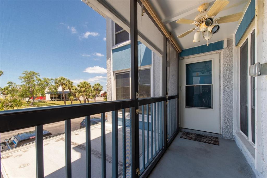 A screened-in balcony with a ceiling fan overlooks a parking area and palm trees — 171 MEDALLION BOULEVARD UNIT F, MADEIRA BEACH, FL