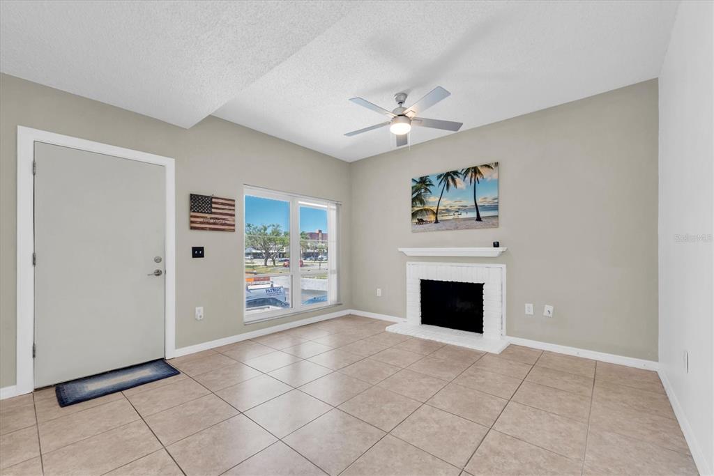 A living room features light tile flooring, a white fireplace, a ceiling fan, and a door — 171 MEDALLION BOULEVARD UNIT F, MADEIRA BEACH, FL