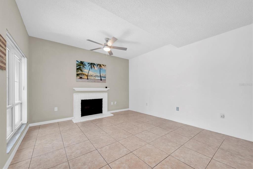 A living room features a fireplace, tile flooring, a ceiling fan, and a beige accent wall — 171 MEDALLION BOULEVARD UNIT F, MADEIRA BEACH, FL