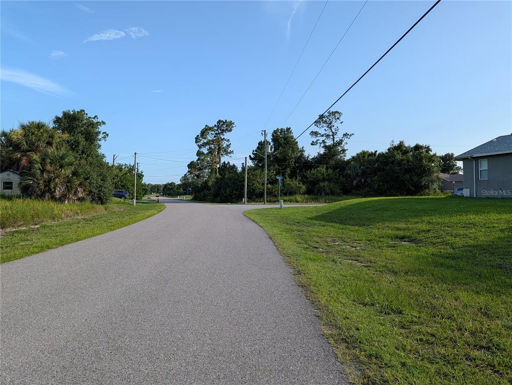 A paved road leads to a T-intersection surrounded by trees and grassy areas — DELWOOD DRIVE, NORTH PORT, FL