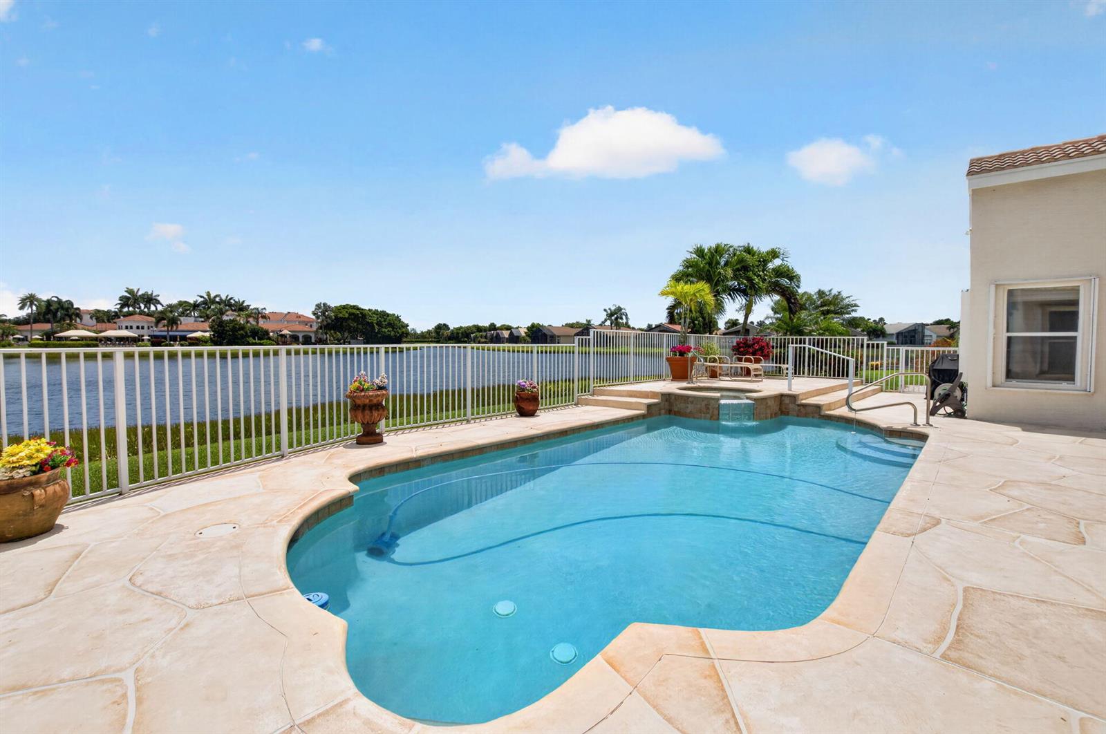 A swimming pool with an attached spa overlooks a lake behind a white fence — 13461 Barcelona Lake Circle, Delray Beach FL 33446, DELRAY BEACH, FL