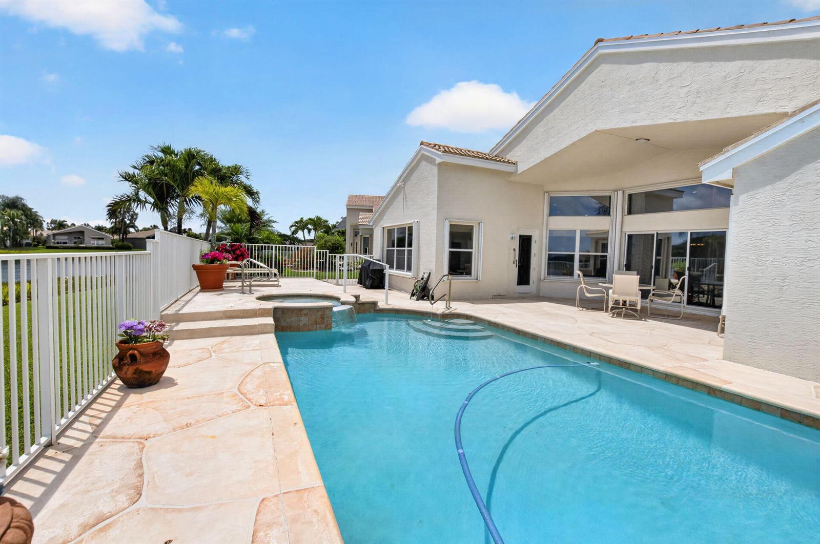 A swimming pool and hot tub sit on a stone patio beside a white house — 13461 Barcelona Lake Circle, Delray Beach FL 33446, DELRAY BEACH, FL