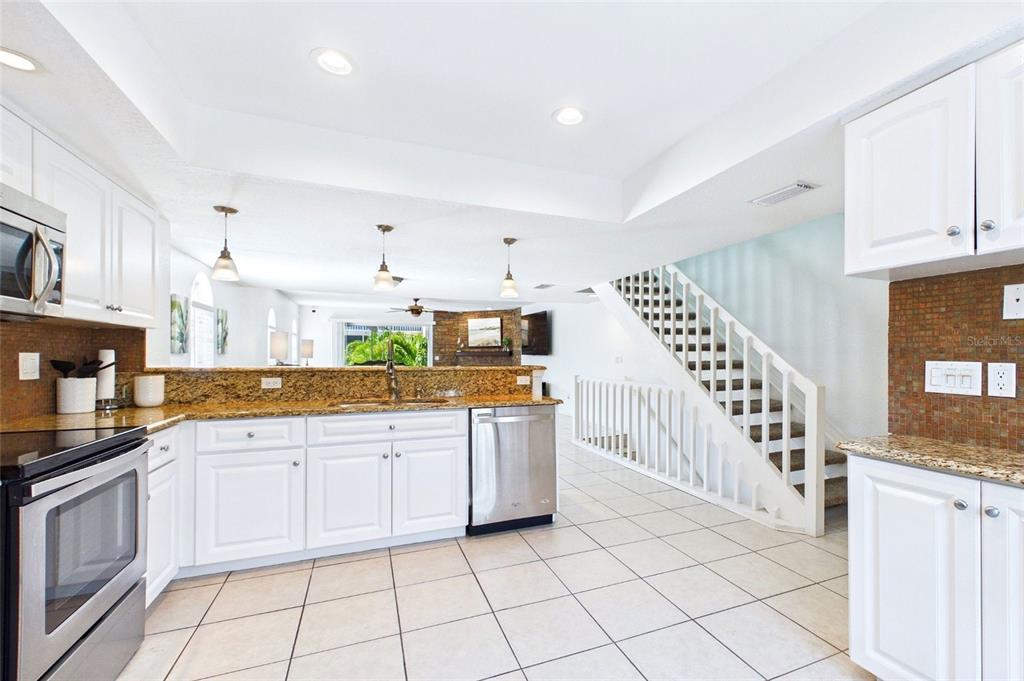 A kitchen with white cabinets, granite countertops, and stainless steel appliances overlooks a living area — 637 PINELLAS BAYWAY S UNIT 301, TIERRA VERDE, FL