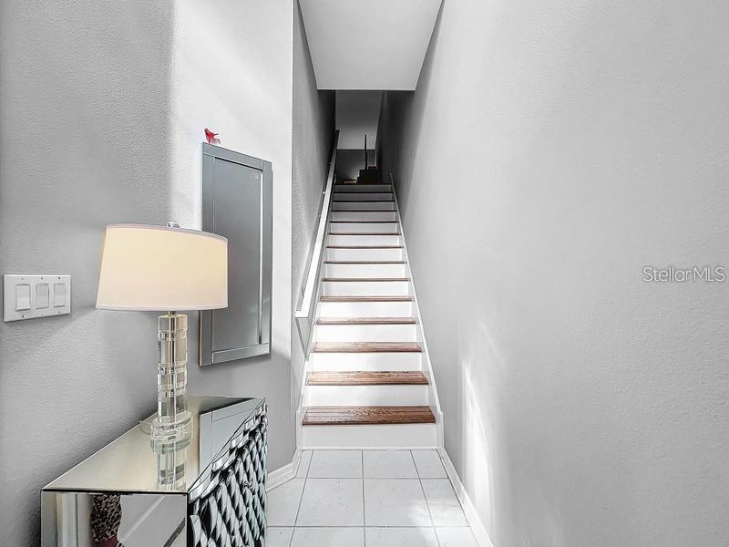A staircase with wooden treads and white risers leads upward from a tiled entryway — 14 SEAGRAPE CIRCLE, CLEARWATER, FL