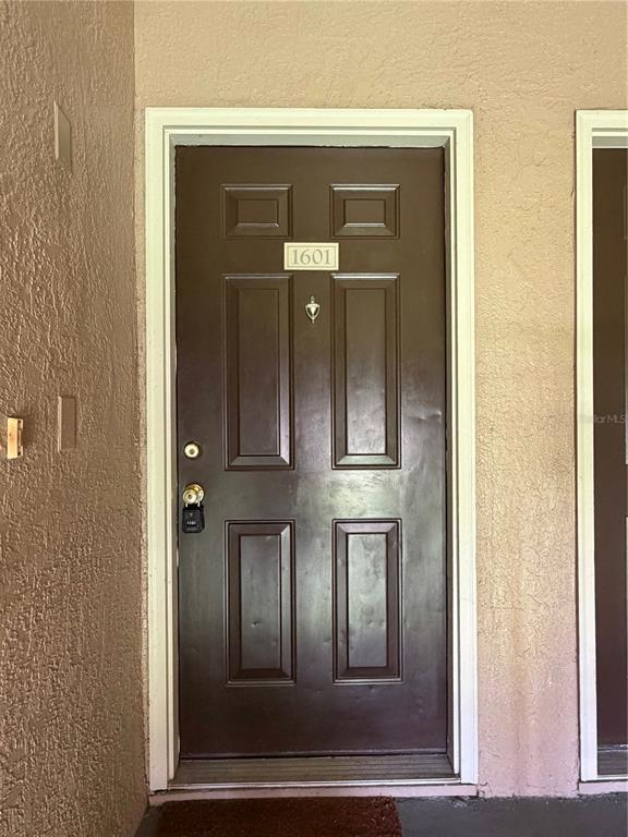A brown front door with a number plate and a lockbox sits in a stucco wall — 14327 FREDRICKSBURG DRIVE UNIT 1601, ORLANDO, FL