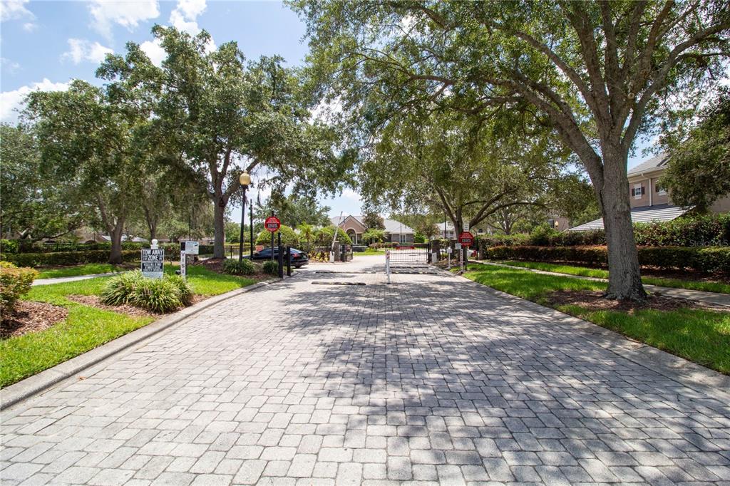A paved driveway leads to a gated residential entrance surrounded by mature trees — 14327 FREDRICKSBURG DRIVE UNIT 1601, ORLANDO, FL