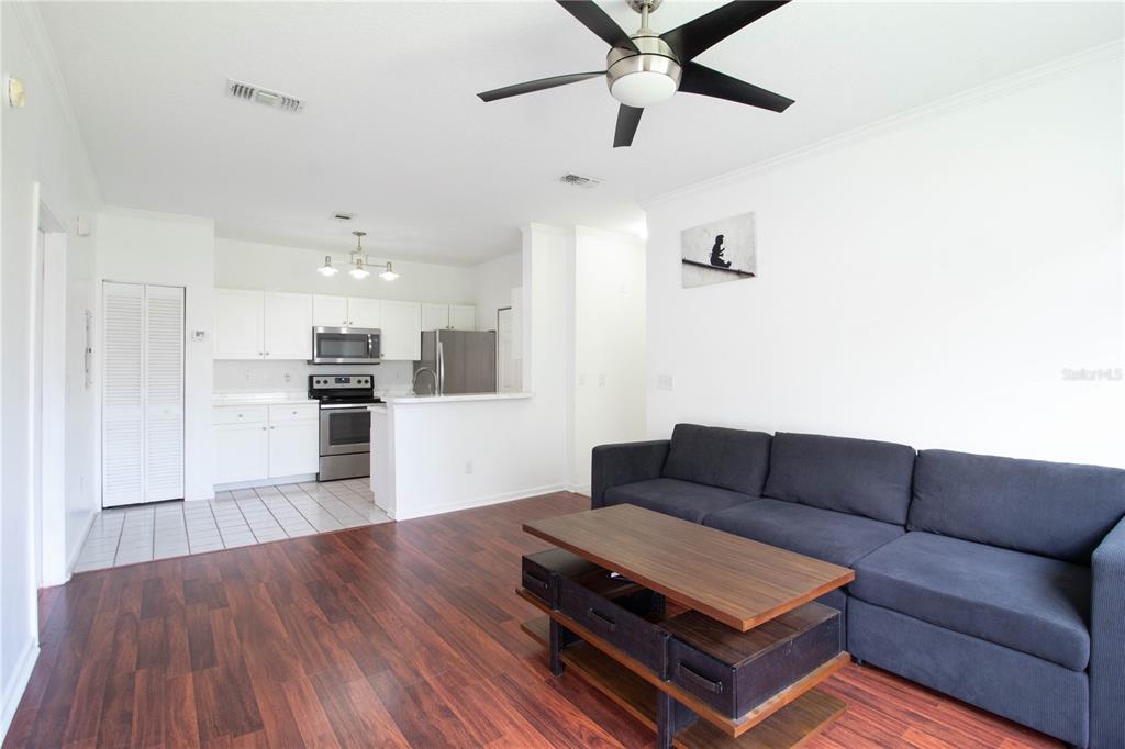 A living room with dark wood floors and a sofa opens to a white kitchen — 14327 FREDRICKSBURG DRIVE UNIT 1601, ORLANDO, FL