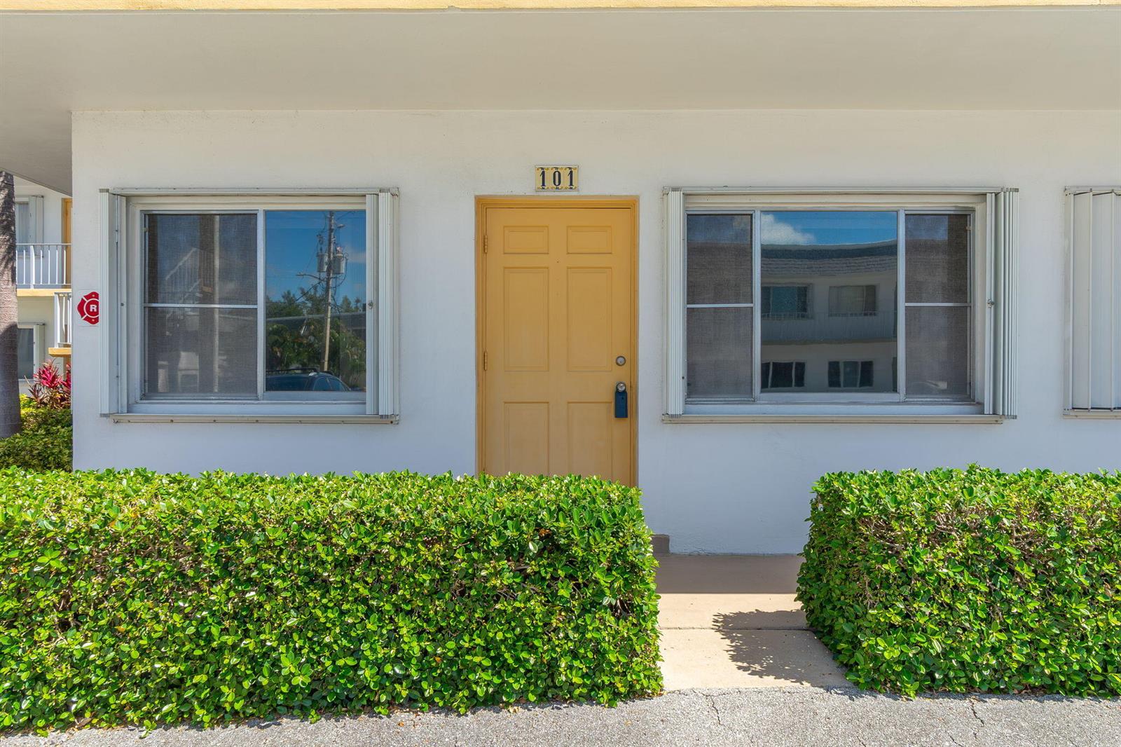 A yellow front door labeled 101 is flanked by two windows and trimmed hedges — 2840 Cynthia Lane # 101, FL 33461, FL