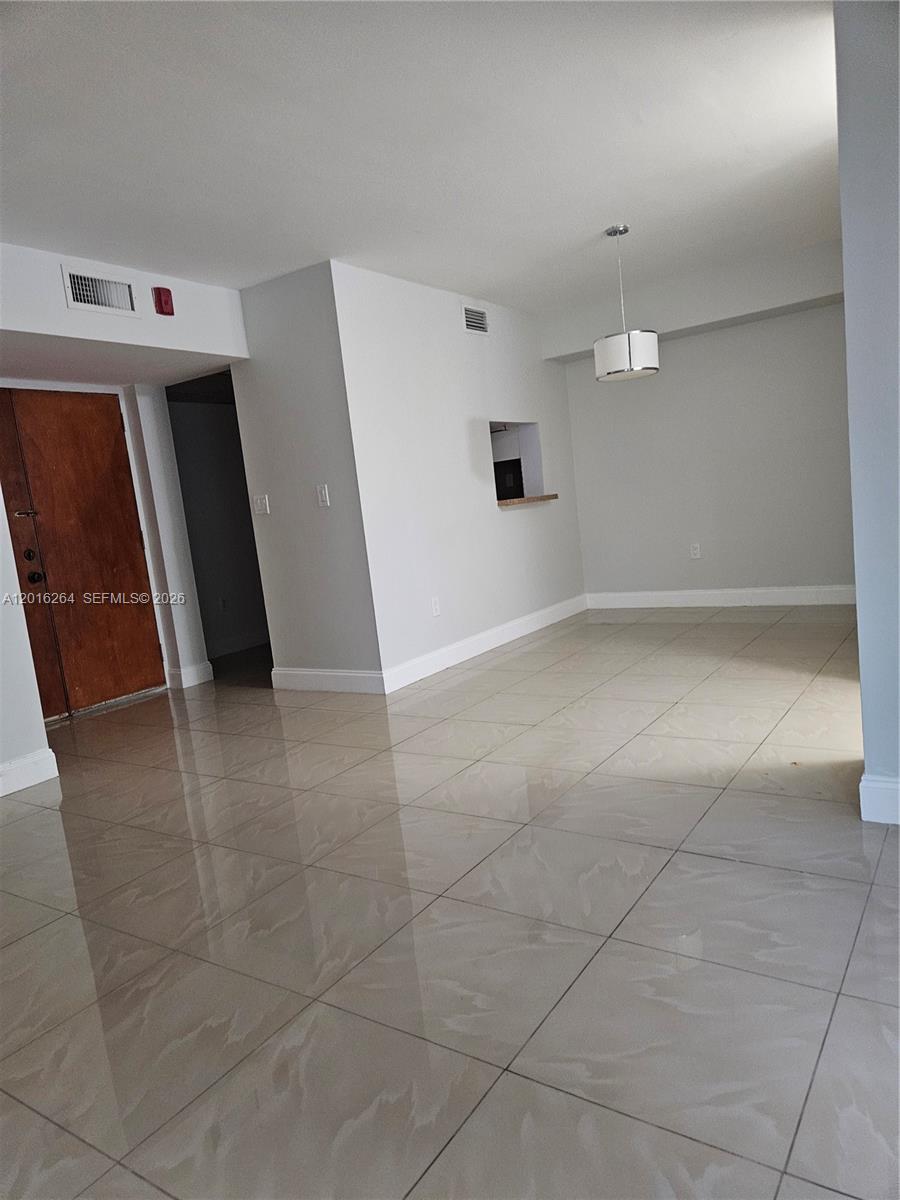 An empty room features large beige floor tiles, white walls, and a hanging pendant light — 11780 SW 18th St # 2, Miami FL 33175, MIAMI, FL