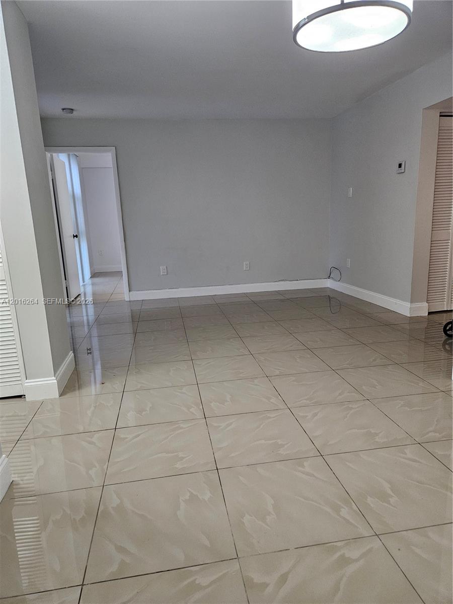 An empty room features light-colored tile flooring, gray walls, and a modern ceiling light fixture — 11780 SW 18th St # 2, Miami FL 33175, MIAMI, FL