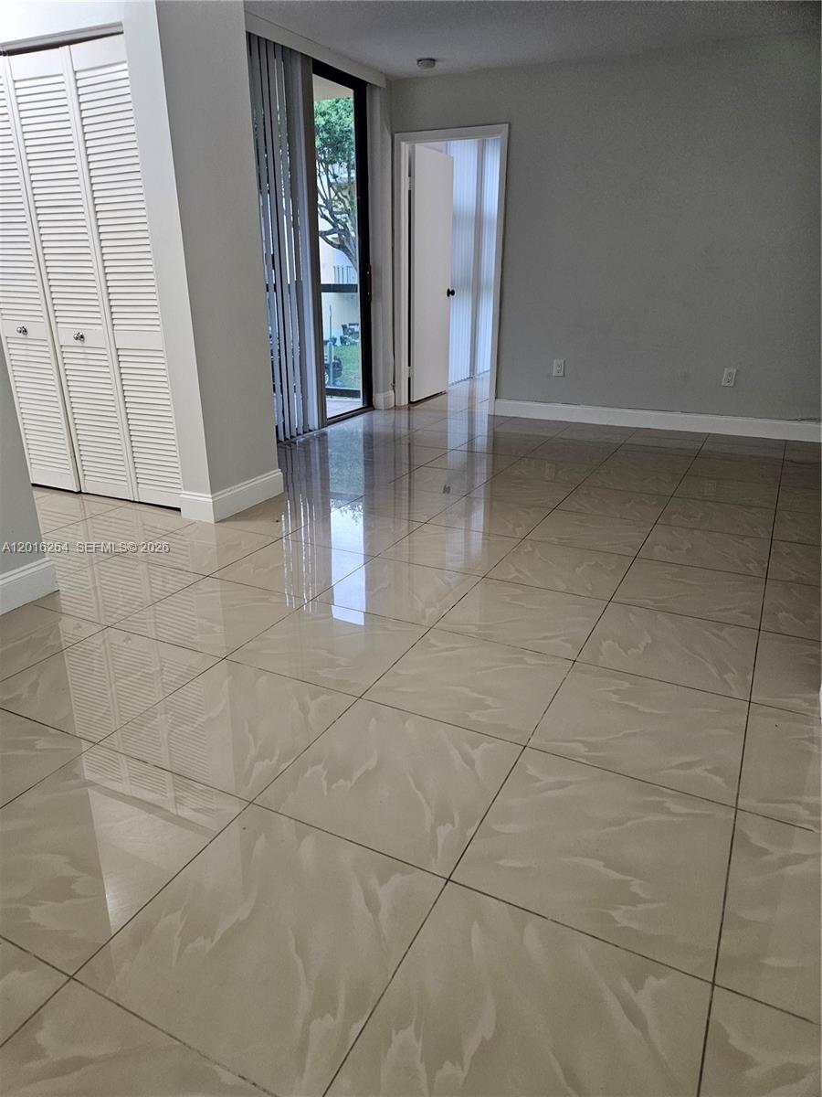 An empty room features glossy beige tile flooring, white louvered closet doors, and a sliding door — 11780 SW 18th St # 2, Miami FL 33175, MIAMI, FL