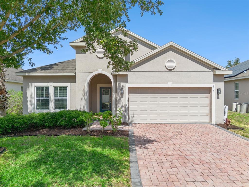 A single-story house with a beige stucco exterior, a two-car garage, and a brick driveway — 457 BRIDGEFORD CROSSING BOULEVARD, DAVENPORT, FL