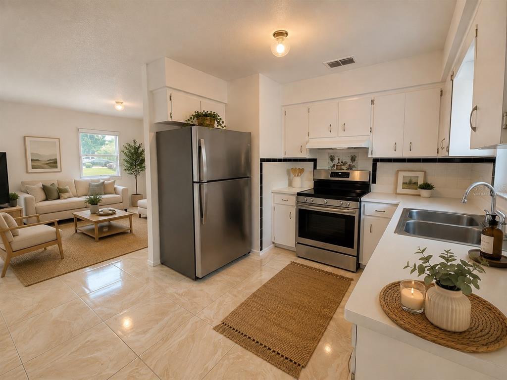 A kitchen with stainless steel appliances and tile flooring opens into a living room area — 206 S 20TH STREET, HAINES CITY, FL