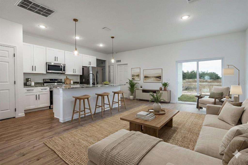 An open-concept kitchen and living area with white cabinets, a kitchen island, and wood flooring — 411 ST JOHNS LANE, KISSIMMEE, FL