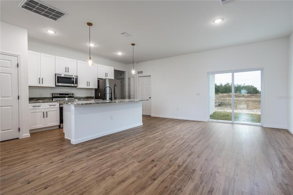A kitchen with white cabinets and a center island opens to a living area — 411 ST JOHNS LANE, KISSIMMEE, FL