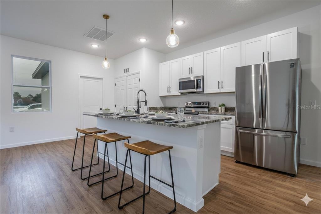 A kitchen features white cabinets, stainless steel appliances, a granite island, and three bar stools — 411 ST JOHNS LANE, KISSIMMEE, FL