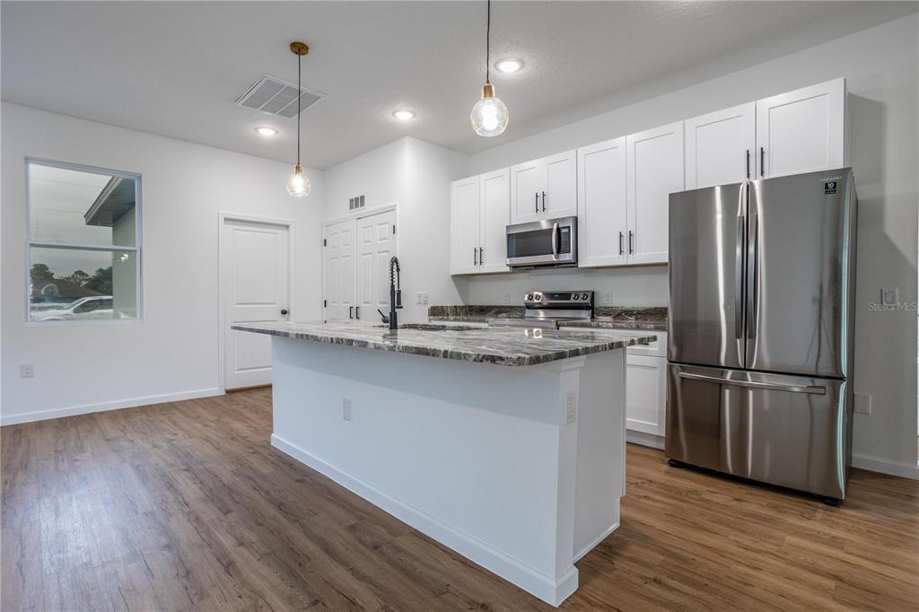 A kitchen features white cabinets, a granite-topped island, stainless steel appliances, and wood-look flooring — 411 ST JOHNS LANE, KISSIMMEE, FL