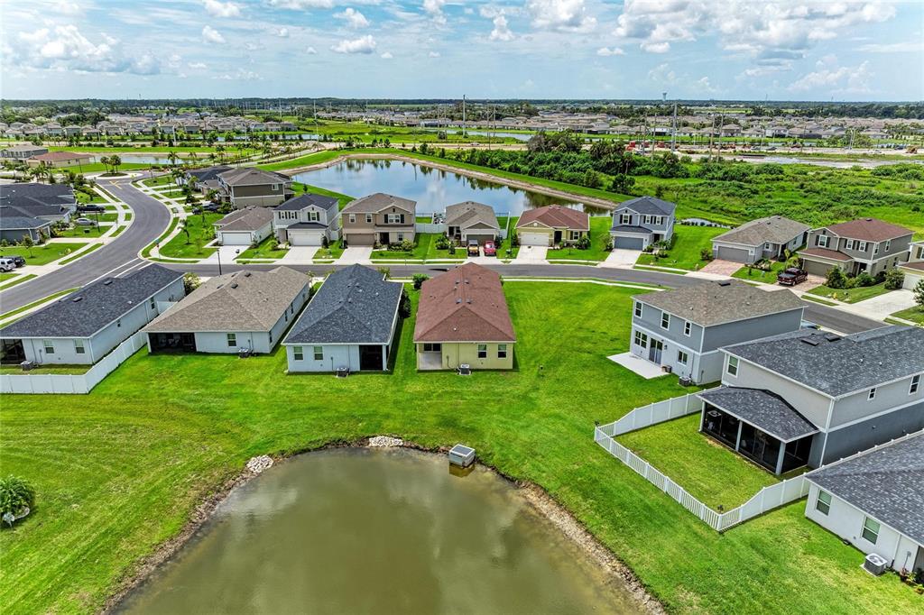An aerial view shows suburban houses with backyards facing a pond under a cloudy sky — 10455 WET MARSH COVE, PARRISH, FL