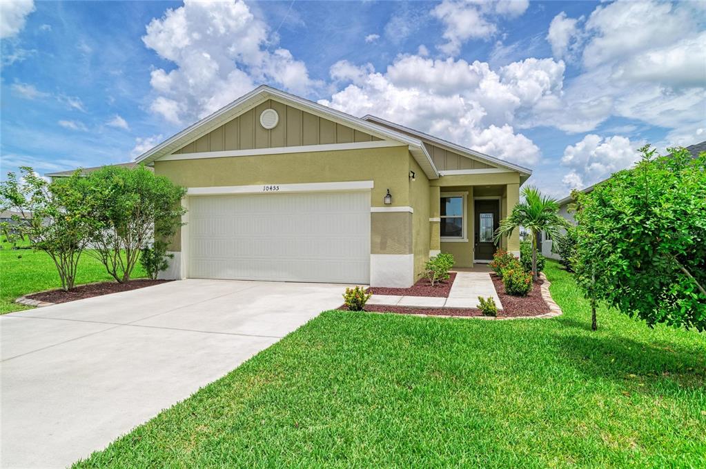 A single-story house with a two-car garage, light green stucco siding, and a concrete driveway — 10455 WET MARSH COVE, PARRISH, FL