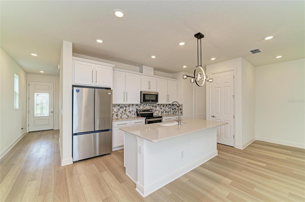 A modern kitchen features white cabinets, stainless steel appliances, a quartz island, and light wood flooring — 10455 WET MARSH COVE, PARRISH, FL