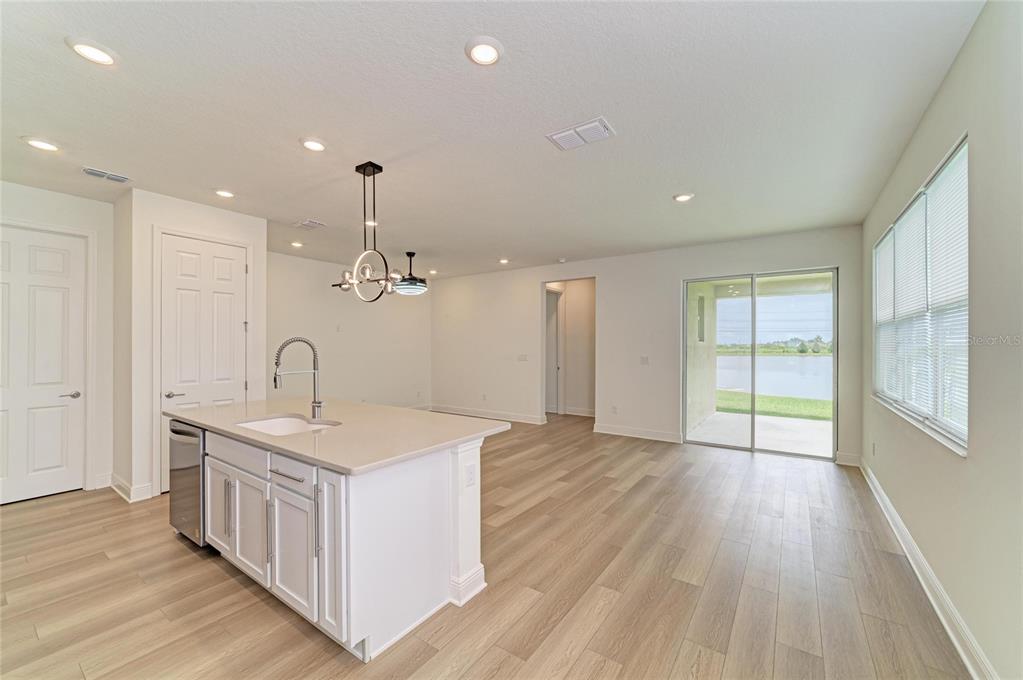 A kitchen island with a sink sits in an open-concept room with wood-look flooring — 10455 WET MARSH COVE, PARRISH, FL