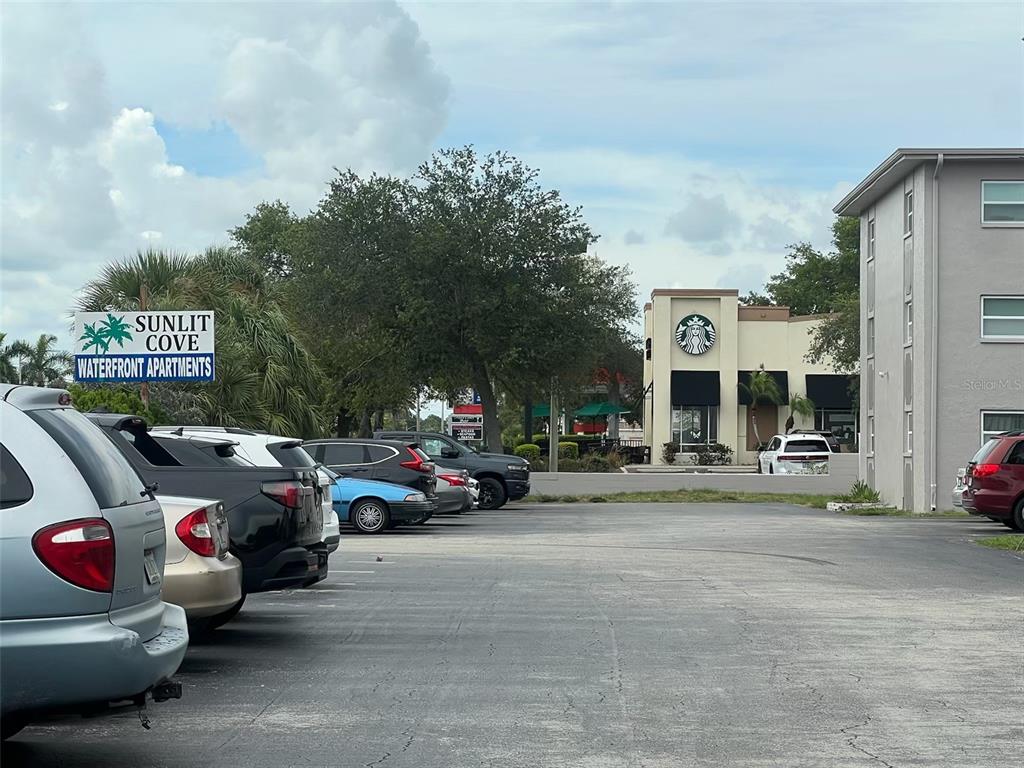 A parking lot sits in front of a Sunlit Cove Waterfront Apartments sign and Starbucks — 8701 4TH STREET N UNIT 105, ST PETERSBURG, FL