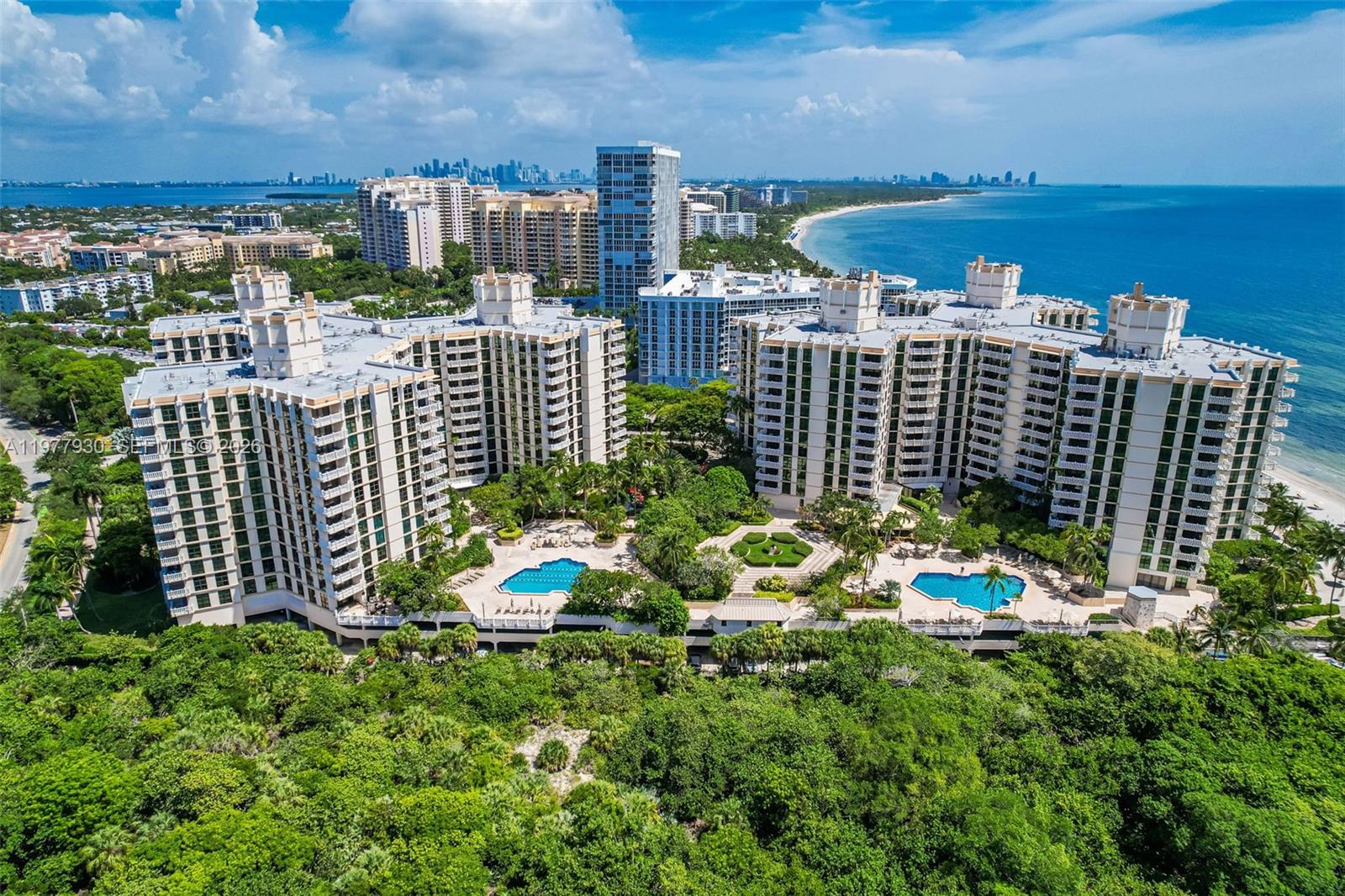 An aerial view shows two large residential buildings with swimming pools surrounded by lush greenery — 1121 Crandon Blvd # E1203, Key Biscayne FL 33149, KEY BISCAYNE, FL