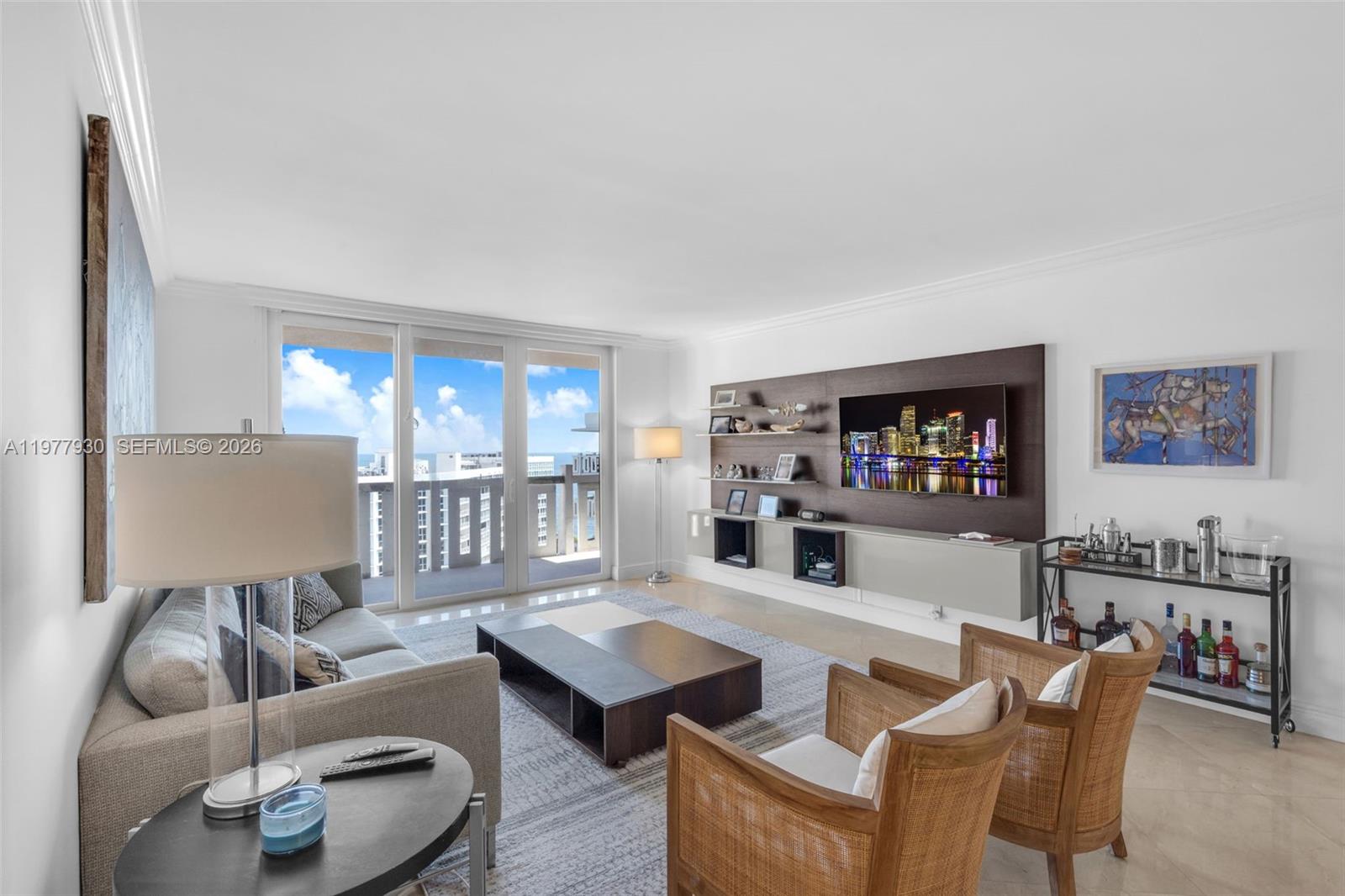 A modern living room features a wall-mounted television, wooden armchairs, and a balcony with ocean views — 1121 Crandon Blvd # E1203, Key Biscayne FL 33149, KEY BISCAYNE, FL