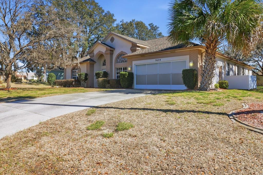 A single-story house with a beige brick facade, a two-car garage, and a palm tree — 5628 W HUNTERS RIDGE CIRCLE, LECANTO, FL