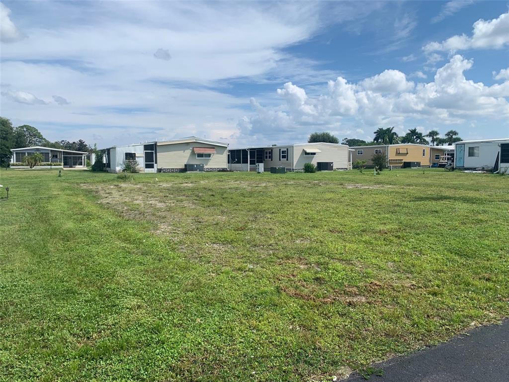 A vacant grassy lot sits in front of several manufactured homes under a cloudy sky — 235 ESTRADA, NORTH PORT, FL