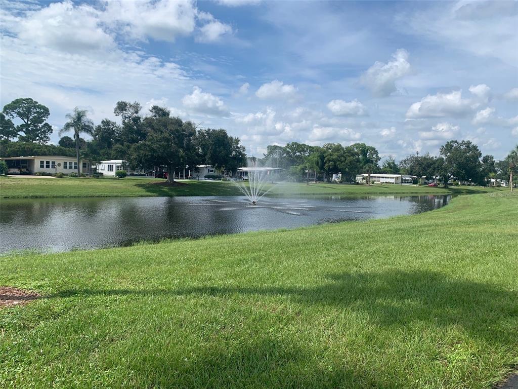 A fountain sprays water in the center of a pond surrounded by grass and houses — 235 ESTRADA, NORTH PORT, FL