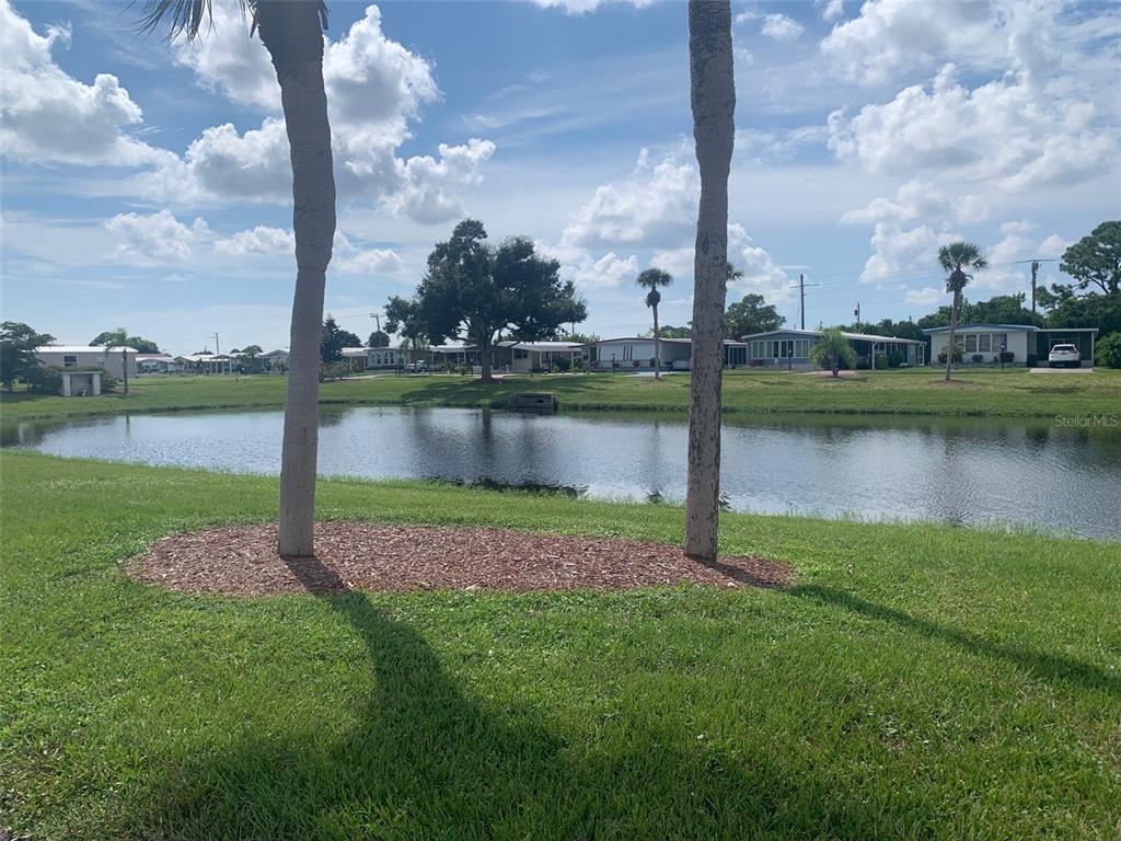 A view of a pond surrounded by grass, palm trees, and several manufactured homes — 235 ESTRADA, NORTH PORT, FL