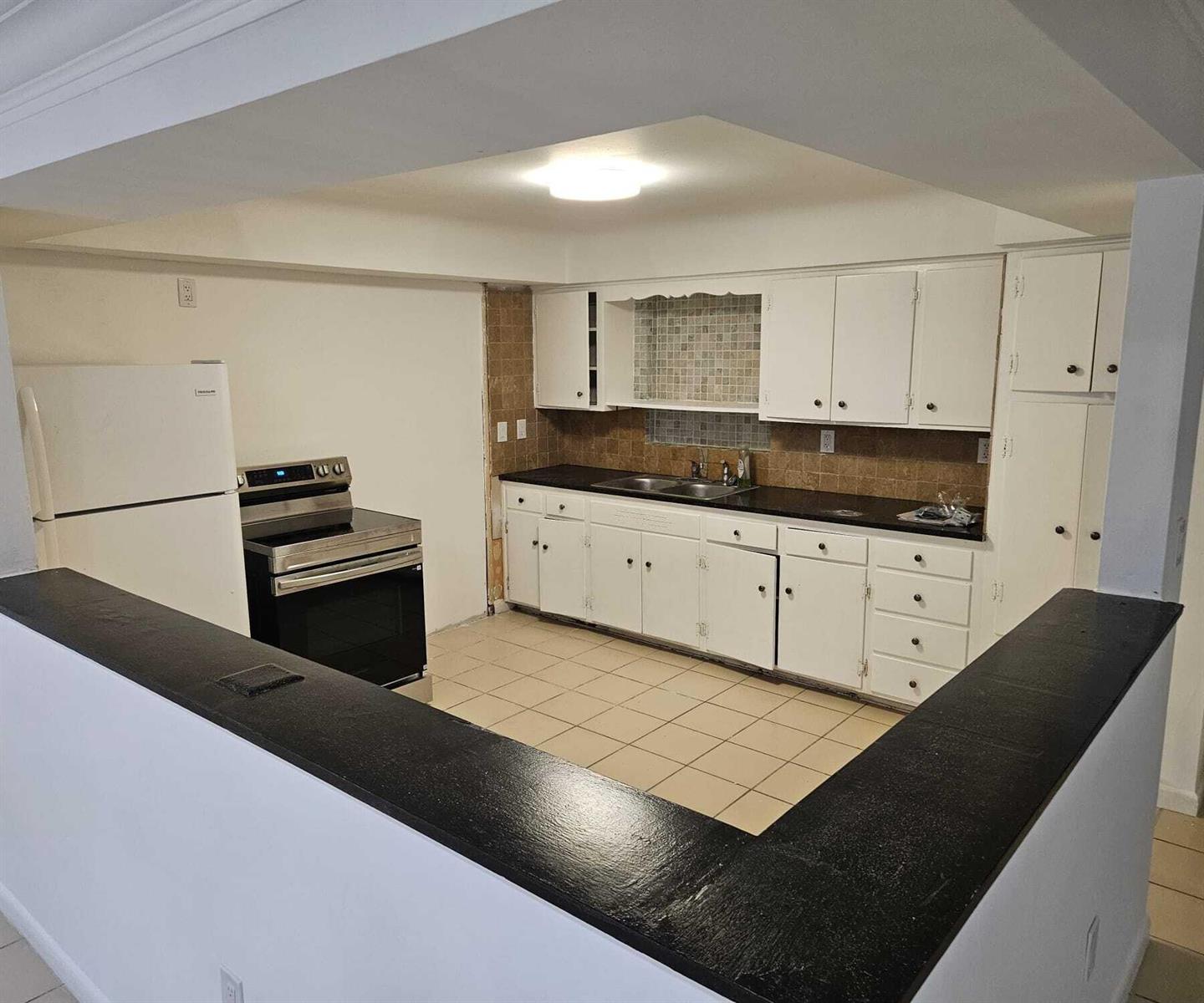 A kitchen with white cabinets, black countertops, a black stove, and a white refrigerator — 1980 Kirk Road, West Palm Beach FL 33406, WEST PALM BEACH, FL