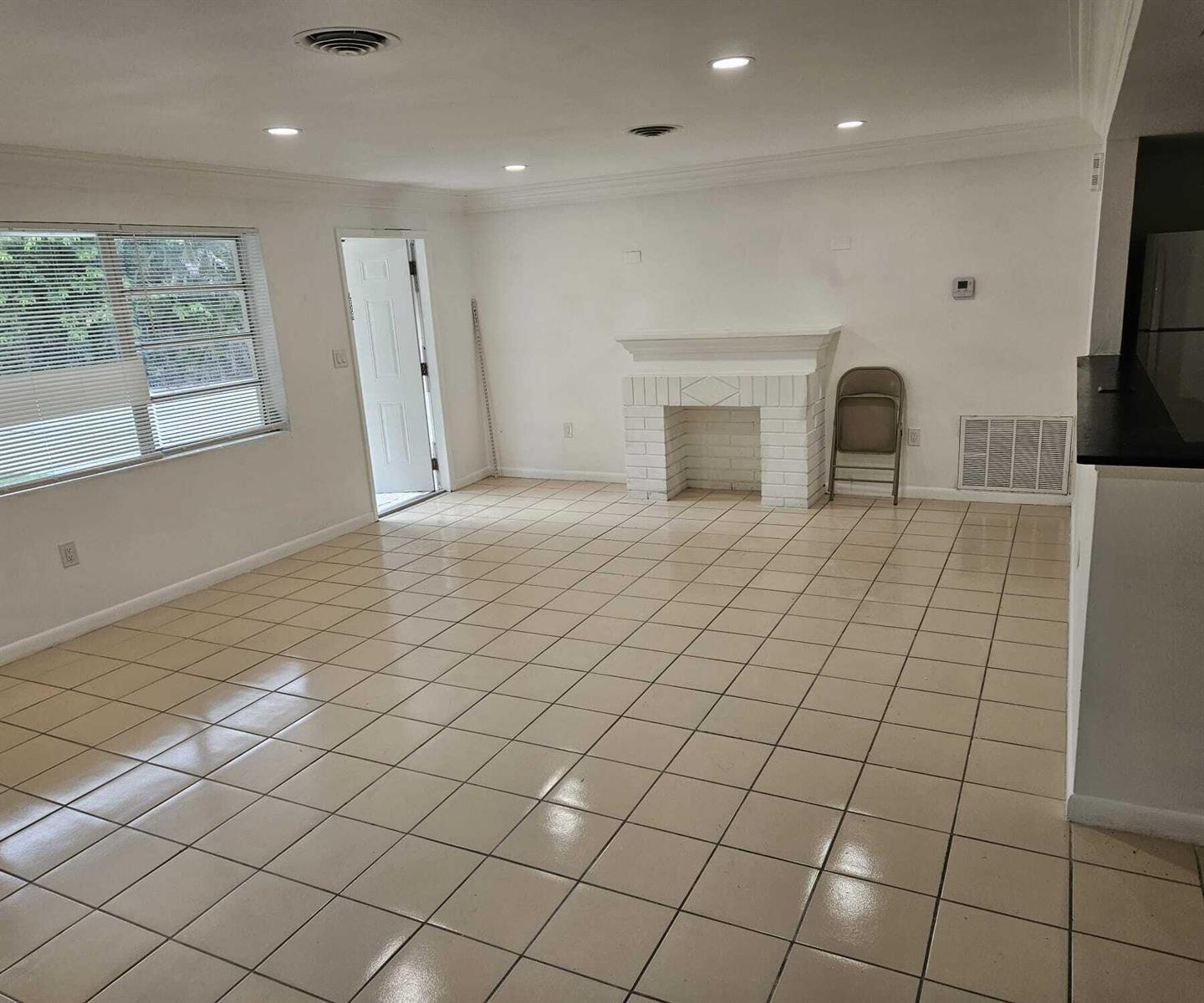 An empty living room features white walls, a white brick fireplace, and light-colored tile flooring — 1980 Kirk Road, West Palm Beach FL 33406, WEST PALM BEACH, FL