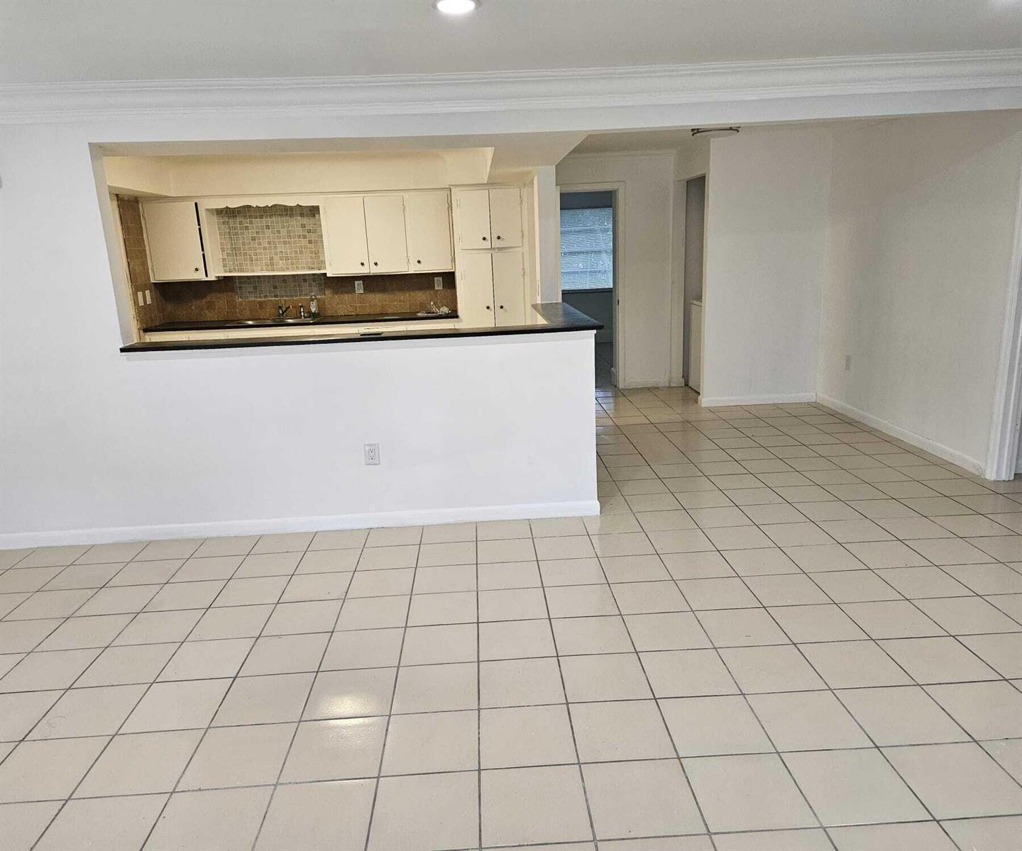 A kitchen with white cabinets and a black countertop overlooks a tiled living area — 1980 Kirk Road, West Palm Beach FL 33406, WEST PALM BEACH, FL