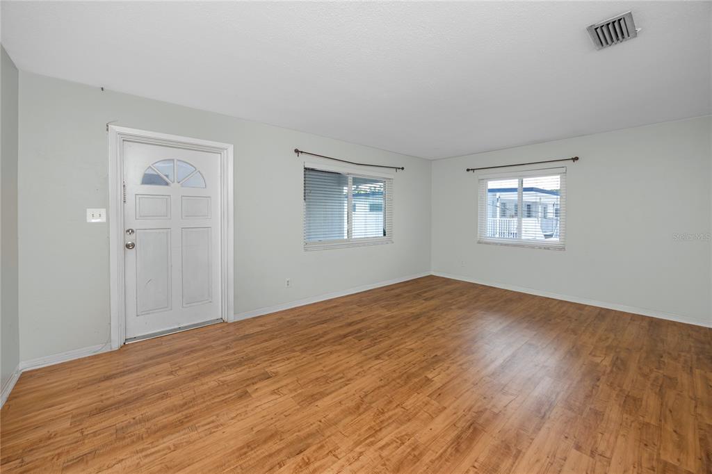 An empty room with light-colored walls, wood-look flooring, two windows, and a white front door — 4340 37TH STREET S UNIT 6, ST PETERSBURG, FL