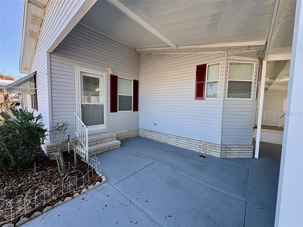 A covered concrete patio area features light gray siding, brick skirting, and a white door — 6086 SOUTHERN OAKS DRIVE SE, WINTER HAVEN, FL