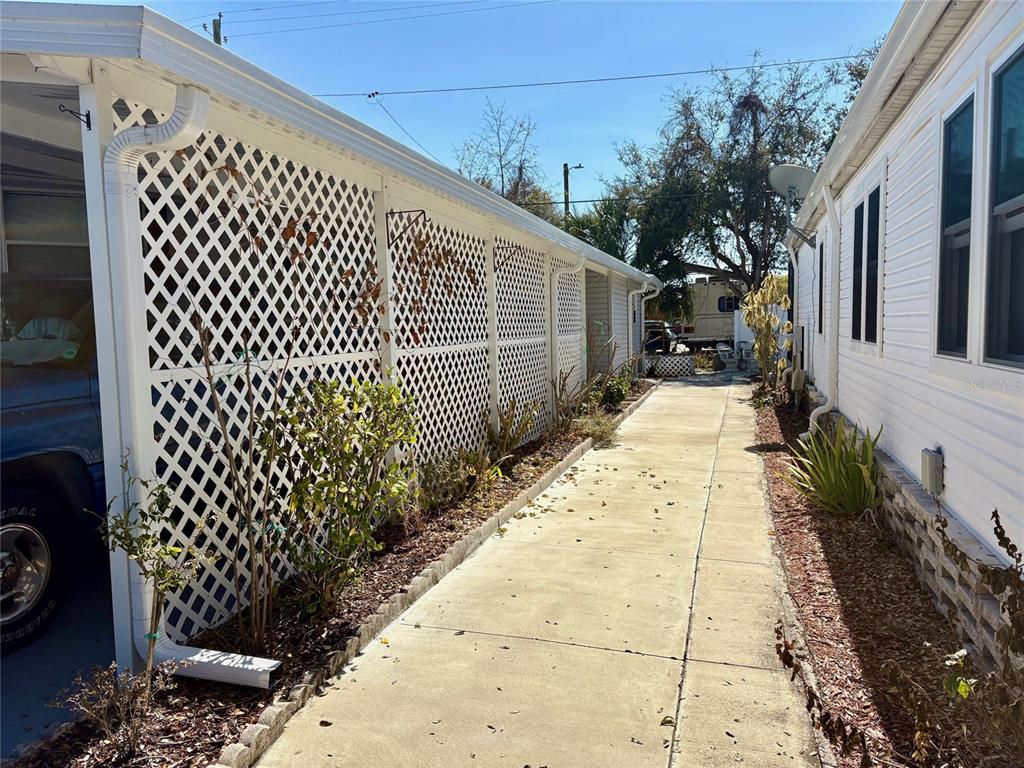 A concrete walkway runs between a white lattice fence and a white mobile home — 6086 SOUTHERN OAKS DRIVE SE, WINTER HAVEN, FL