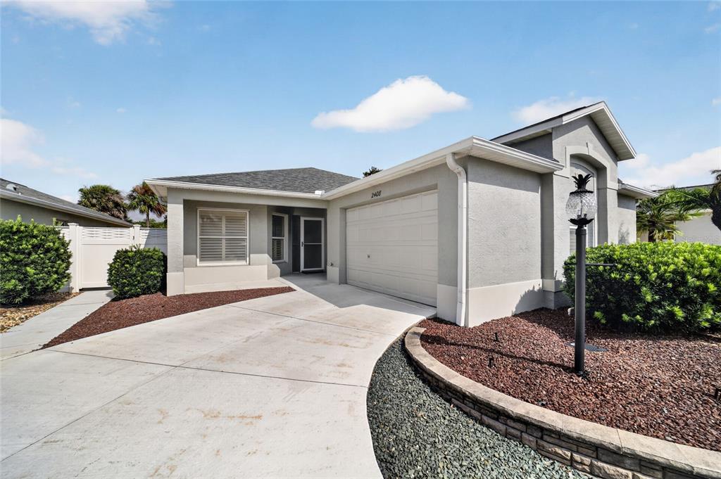A single-story house with a gray stucco exterior, a two-car garage, and a concrete driveway — 2408 SAFFRON LANE, THE VILLAGES, FL