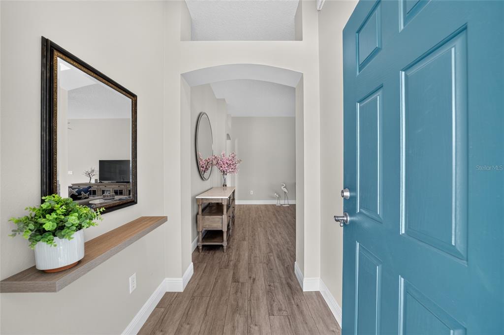 An entryway features a blue door, wood-look flooring, a floating shelf, and a wall mirror — 2408 SAFFRON LANE, THE VILLAGES, FL
